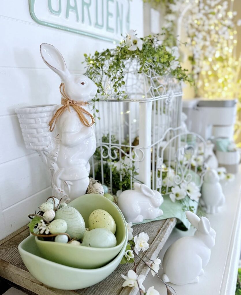 A white decorative birdcage with a white bunny figurine and green Easter eggs.