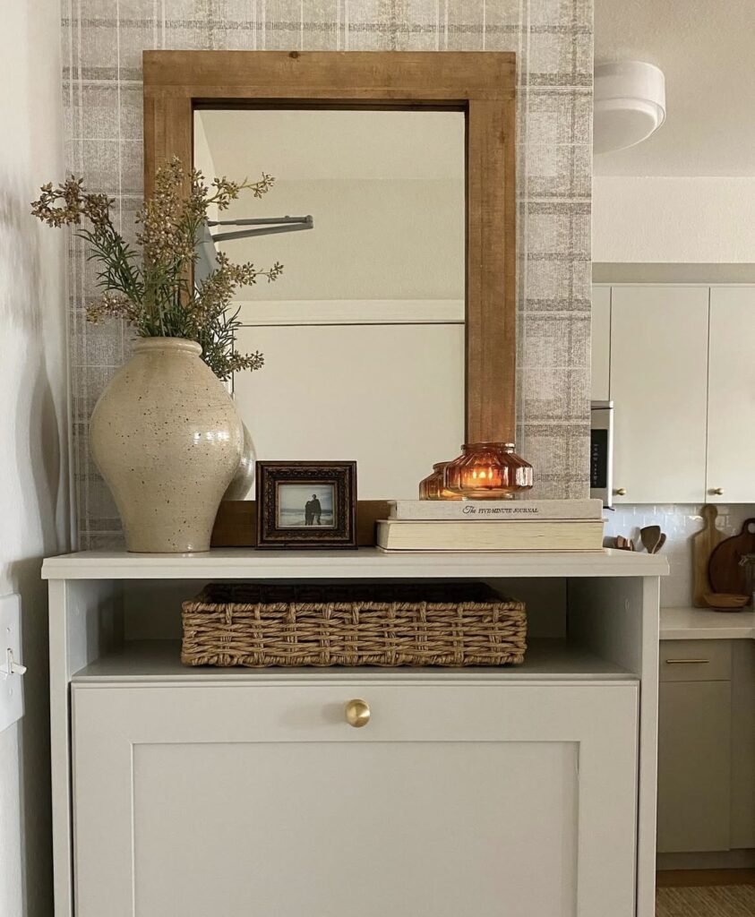 A small entryway with a large wooden mirror, decorative books and a ceramic vase.