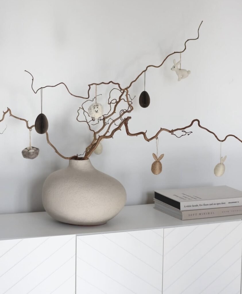 A beige ceramic vase with curly branches and Easter ornaments.