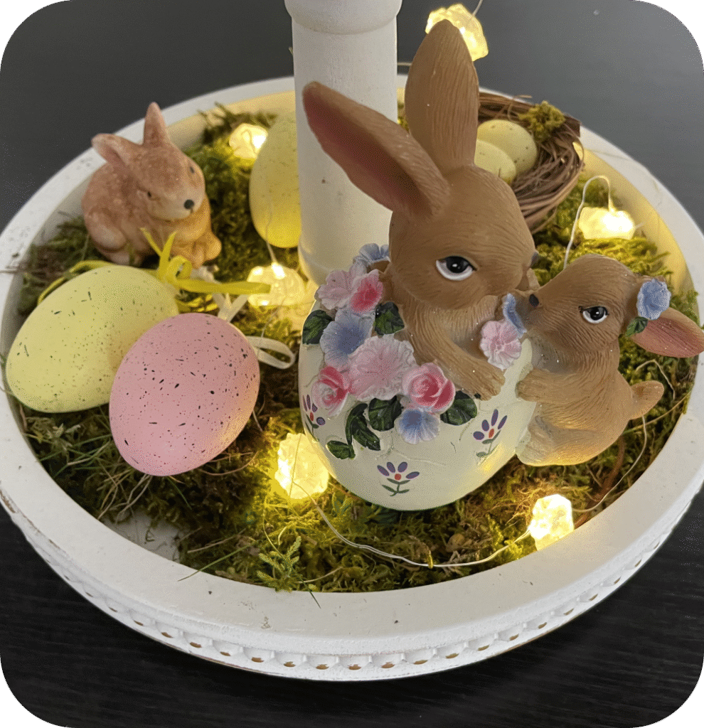 An Easter tiered tray with moss, bunny figurines, Easter eggs, and string lights.