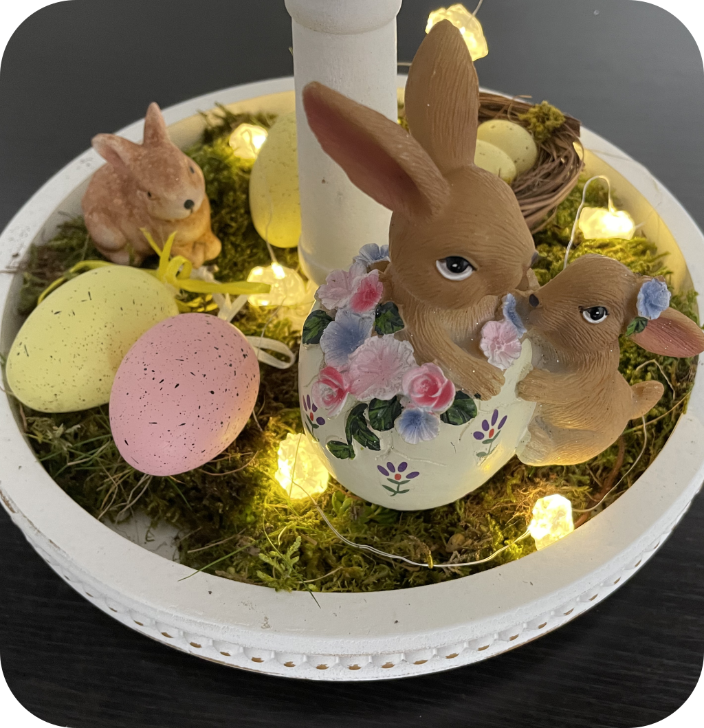 An Easter tiered tray with moss, bunny figurines, Easter eggs, and string lights.