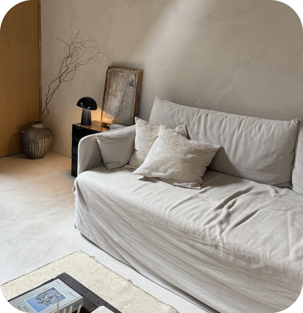 A Scandinavian living room with a white sofa, a black lamp, and a ceramic vase filled with curly branches.