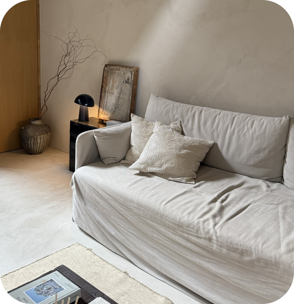 A Scandinavian living room with a white sofa, a black lamp, and a ceramic vase filled with curly branches.